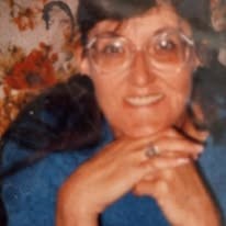 Becky Schlief smiling, wearing glasses and a blue sweater, her hands folded under her chin