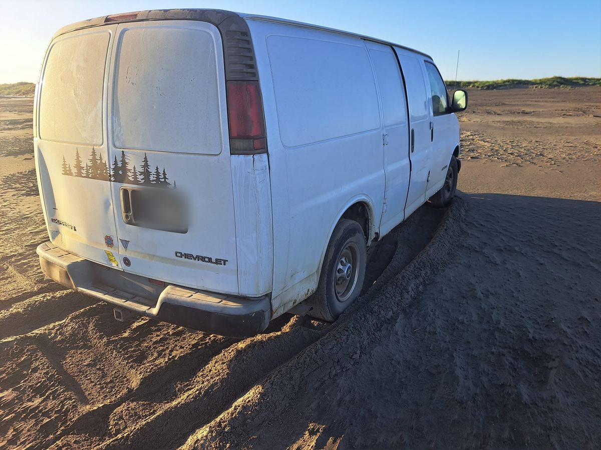 The white Chevy Express van parked on a sandy beach at golden hour
